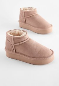 Rosa mockaskinnsankelstövlar med en mjuk, pälsfoder och bred fotöppning. Tjock, texturerad gummisula med en lätt platå. Sömnadsdetaljer synliga.