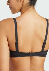 Čierna podprsenka s nastaviteľnými tenkými ramienkami a zapínaním na háčik. Hladká látka s minimálnymi detailmi a bezšvovým dizajnom vzadu.