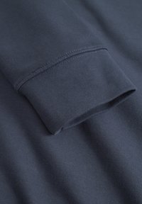 Navy blue long-sleeve shirt cuff with a smooth texture, featuring clean stitching and a fitted design. Material appears soft and stretchy.