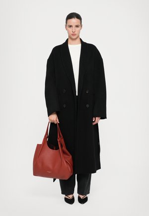 Black wool double-breasted coat, white top, and dark jeans. Holding a large, textured red leather handbag. Black pointed flats.