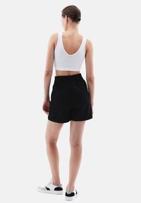 Pantaloni shorts neri con vita elasticizzata e una vestibilità comoda, abbinati a un top corto bianco a coste con un ampio scollo sulla schiena.