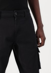 Schwarze Cargo-Hose aus Baumwolle, mit Seitentaschen, vorderer Knopfverschluss und geradem Bein-Design mit glatter Textur.