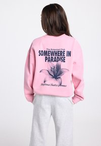 Roze sweatshirt met een grafische print van een lelie en de tekst "Somewhere in Paradise" en "The Botanical Club." Comfortabele pasvorm, losse mouwen.