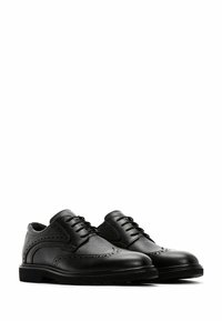 Chaussures de brogue en cuir noir avec un capuchon lisse, un dessus texturé, des détails en forme d'aile et des lacets contrastants sur une semelle en caoutchouc basse.