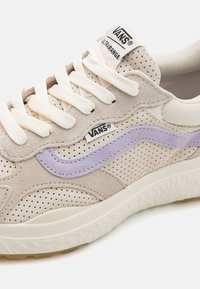 Vans-sneakers har en beige perforert suede overdel med en lavendelstripe, kremfargede snørebånd og en strukturert hvit gummisåle.