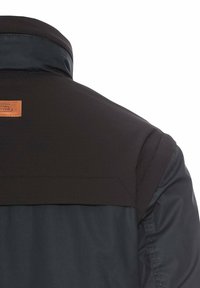 Sort og mørkeblå jakke med en struktureret krave, glat tekstur og en brun læderlap detalje øverst på ryggen.