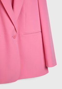 Blazer rose avec une fermeture à un bouton, un col cranté et une poche passepoilée horizontale sur le devant droit.
