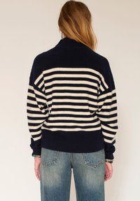 Pull rayé bleu marine et crème avec col roulé et épaules tombantes, fabriqué en tissu doux. Assorti à un jean en denim bleu taille haute.