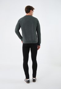Sudadera de cuello redondo en verde oscuro, con tejido suave, puños y bajo acanalados, combinada con pantalones ajustados negros y zapatos casuales en blanco y negro.