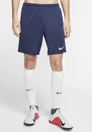 Pantaloni corti blu navy Nike con logo Swoosh bianco, abbinati a calze bianche al ginocchio e calzature grigio-rosse, caratterizzati da un design minimalista.