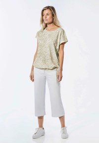 Lichtgroene, gestreepte top met korte mouwen, een relaxte pasvorm en een trekkoordzoom, gecombineerd met witte cropped broek en witte sneakers.