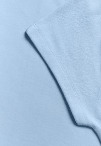 Lyseblå bomulds t-shirt med en glat tekstur og rund hals. Har korte ærmer, der overlapper et andet lag i samme farve.