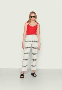 Top vermelho com alças ajustáveis, combinado com calças largas brancas com riscas em tie-dye preto. Sandálias pretas completam o visual.