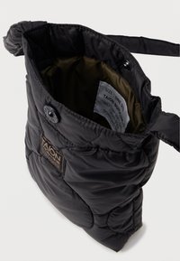 Černá prošívaná taška přes rameno s lesklým povrchem, s uzavíráním na knoflík a vnitřní štítek s informacemi o velikosti a péči.