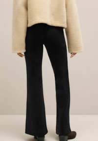 Schwarze, ausgestellte Hosen aus weichem Stoff mit glatter Textur und hohem Taillen Design, kombiniert mit einem beigen, flauschigen, übergroßen Oberteil.