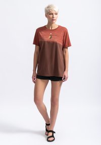 Korte mouwen, ronde hals t-shirt in roestig oranje en bruin, met een grafische print op de bovenborst. Zachte katoen stof; ontspannen pasvorm.