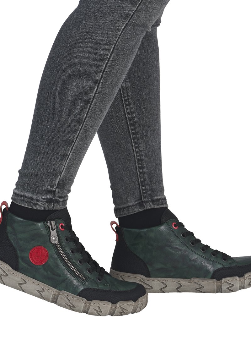 Baskets montantes en cuir vert foncé avec un panneau noir texturé. Elles présentent une fermeture éclair sur le côté, des accents rouges et une semelle épaisse et à motifs.