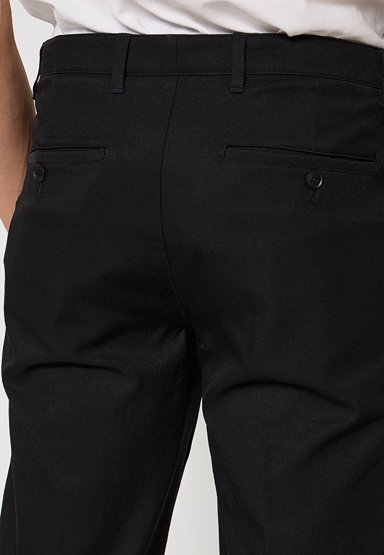Pantalon noir en tissu lisse avec une coupe ajustée. Doté de deux poches arrière avec des fermetures à bouton et d'une taille classique.