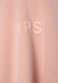 Růžová pletená tkanina s vystouplými světle růžovými písmeny "YPS" uspořádanými horizontálně přes povrch.