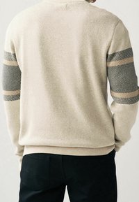 Maglione a maglia beige con maniche testurizzate a contrasto, caratterizzato da un motivo a spina di pesce e strisce beige chiaro. Vestibilità slim e polsini a costine.