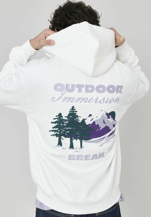 Hoodie blanc avec un design graphique présentant des montagnes violettes et des arbres verts. Texte "IMMERSION EN PLEIN AIR" et "PAUSE" dans des couleurs complémentaires.