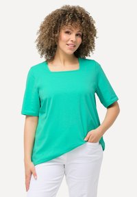 Top turchese a maniche corte con scollo quadrato, realizzato in un tessuto morbido. Abbinato a pantaloni bianchi, dotato di una vestibilità comoda.