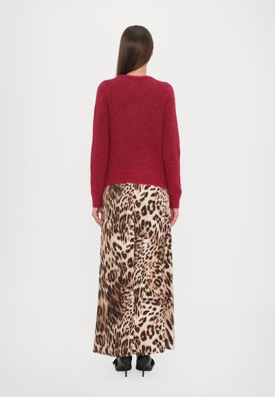 Maglione rosso a maglia con texture abbinato a una lunga gonna leopardata. L'outfit presenta una vista posteriore, mettendo in risalto la sua silhouette fluida.