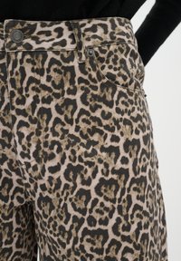 Pantalons en denim à imprimé léopard avec des tons beige et noir, dotés d'une taille haute, d'une poche avant et d'une quincaillerie en métal. Tissu texturé.