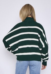 Green striped knit sweater with white horizontal lines, loose fit, high collar, and textured fabric. Worn with light blue denim jeans.