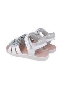 Sandalias infantiles blancas con acentos plateados, suela plana, diseño de punta abierta y detalle de lazo en la correa. Fabricadas con materiales sintéticos.