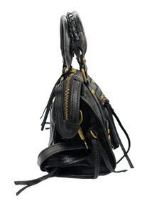 Sac à main en cuir noir avec une finition texturée, comportant des matériaux en or, un compartiment zippé et des poignées tressées. La vue de côté montre les détails.