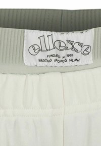 Ellesse-Loge auf dem weißen elastischen Bund eines gerippten, hellgrauen und weißen Kleidungsstücks.
