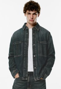 Donker was denimjack, met knoopsluiting, twee borstzakken en een klassieke kraag. Lichtgewicht met zichtbare stikseldetails.