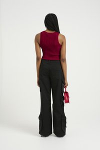Red ribbed knit crop top with black cargo pants featuring multiple pockets and a loose fit, holding a small red handbag.