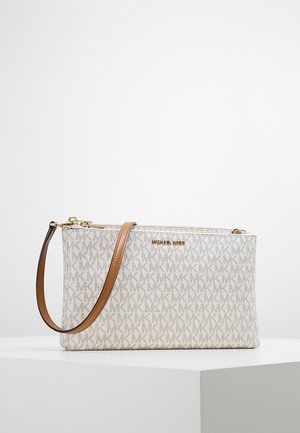 Kleine rechthoekige beige schoudertas met herhaald "MK"-patroon, gouden rits en verstelbare bruine leren riem op een witte ondergrond.