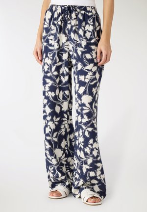 Pantaloni larghi blu navy con motivi floreali bianchi, vita elastica con coulisse, indossati con sandali bianchi e una maglietta bianca.