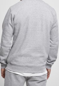 Sudadera gris con puños y dobladillo acanalados, hecha de una tela suave. Presenta un clásico escote de cuello redondo, exhibiendo un diseño simple y sin adornos.