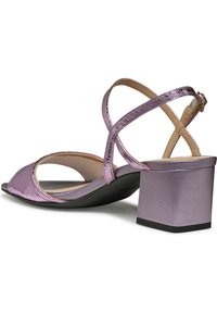 Sandalia de tacón alto metálica morada con diseño de tiras cruzadas, punta descubierta y tacón cuadrado. Superficie texturizada con acentos suaves.