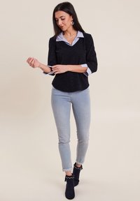 Haut noir texturé avec un col bleu et des manches trois-quarts, associé à un jean skinny bleu clair et des bottines navy avec des franges.