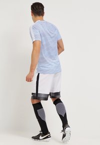 Camiseta de rayas azules, pantalones cortos blancos con detalles en negro y calcetines de fútbol negros. Material ligero y ajuste atlético diseñado para el deporte.