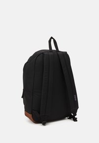 Zaino nero con spallacci imbottiti, forma arrotondata e un accento in pelle marrone sul fondo. Presenta una tasca laterale e un manico superiore per il trasporto.