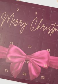 Adventikalender sügavale burgundia taustale, kuldsete tähtedega, nummerdatud akendega ja suure roosa satiinipaelaga, mis on silmapaistvalt esile tõstetud.