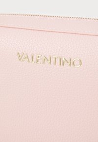 Pochette in pelle texture rosa chiaro con logo dorato "VALENTINO". Presenta una cerniera superiore e cuciture dettagliate lungo il bordo.