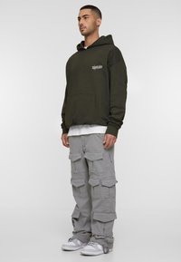 Olive green hoodie with a front pocket and print, paired with light grey cargo pants featuring multiple pockets and a relaxed fit.