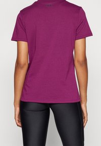 Fialové tričko s krátkým rukávem z pohledu zezadu, vyrobené z bavlny, s kulatým výstřihem a jemným logem u límce.
