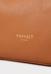 Brązowa skórzana torba o teksturowanej powierzchni, z wytłoczonym na złoto logo "TWINSET MILANO". Prosty design bez dodatkowych akcentów.