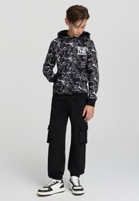 Felpa con cappuccio a motivo marmo in bianco e nero, dotata di tasca frontale, abbinata a pantaloni cargo neri con tasche laterali e polsini elasticizzati.