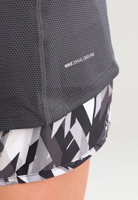 Top Nike Zonal Cooling in tessuto mesh grigio con superficie testurizzata; i pantaloni corti inferiori presentano un motivo geometrico bianco e nero e una finitura liscia.