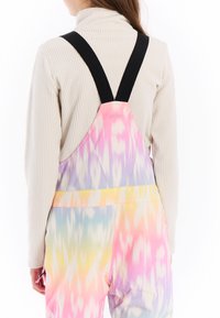 Pestré sněhové kombinézy s tie-dye vzorem v odtieňoch ružovej, žltej a modrej, s čiernymi nastaviteľnými popruhmi.