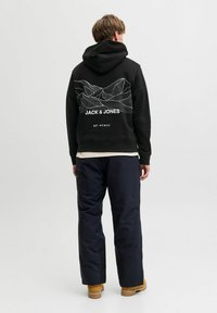 Czarna bluza z kapturem z białą grafiką gór i napisem "JACK & JONES" na plecach. Noszona z granatowymi spodniami i brązowymi butami.